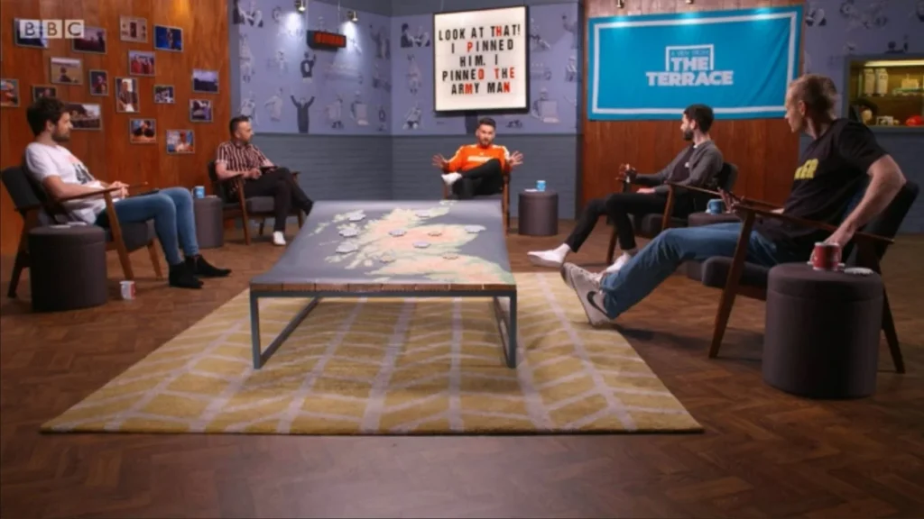 Men in studio discuss "Period Props" with map table and BBC logo.