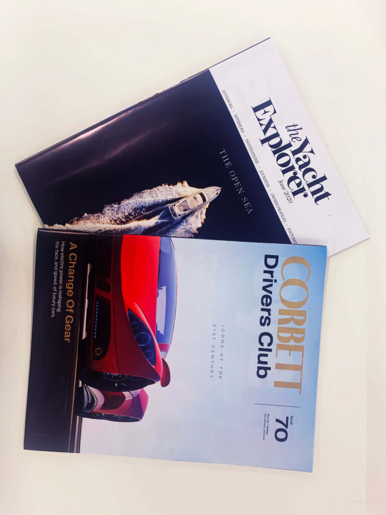 Two luxury yacht and car magazines, "The Yacht Explorer" and "Corbett Drivers Club
