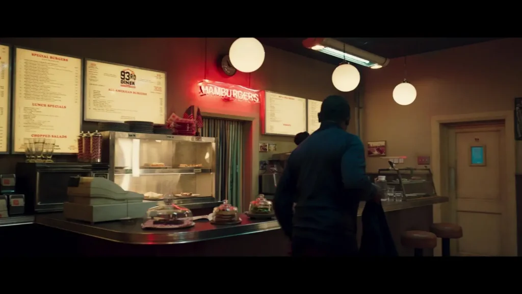 Diner interior with "HAMBURGERS" sign, screens, and patrons