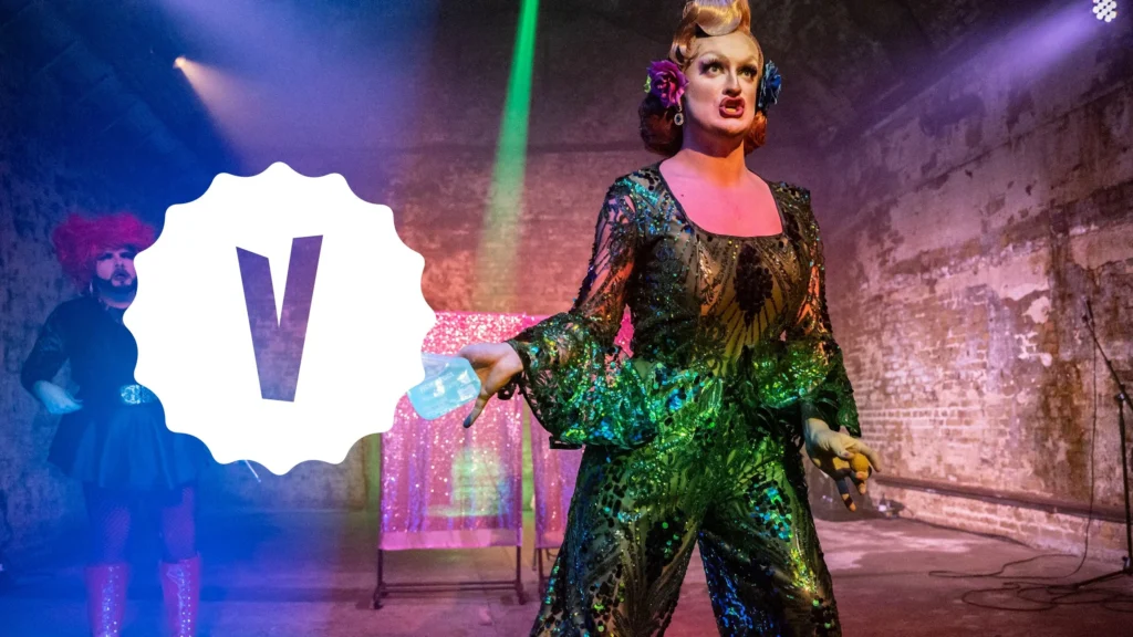 Drag performer in a green sequined outfit on stage, with a V logo overlay.