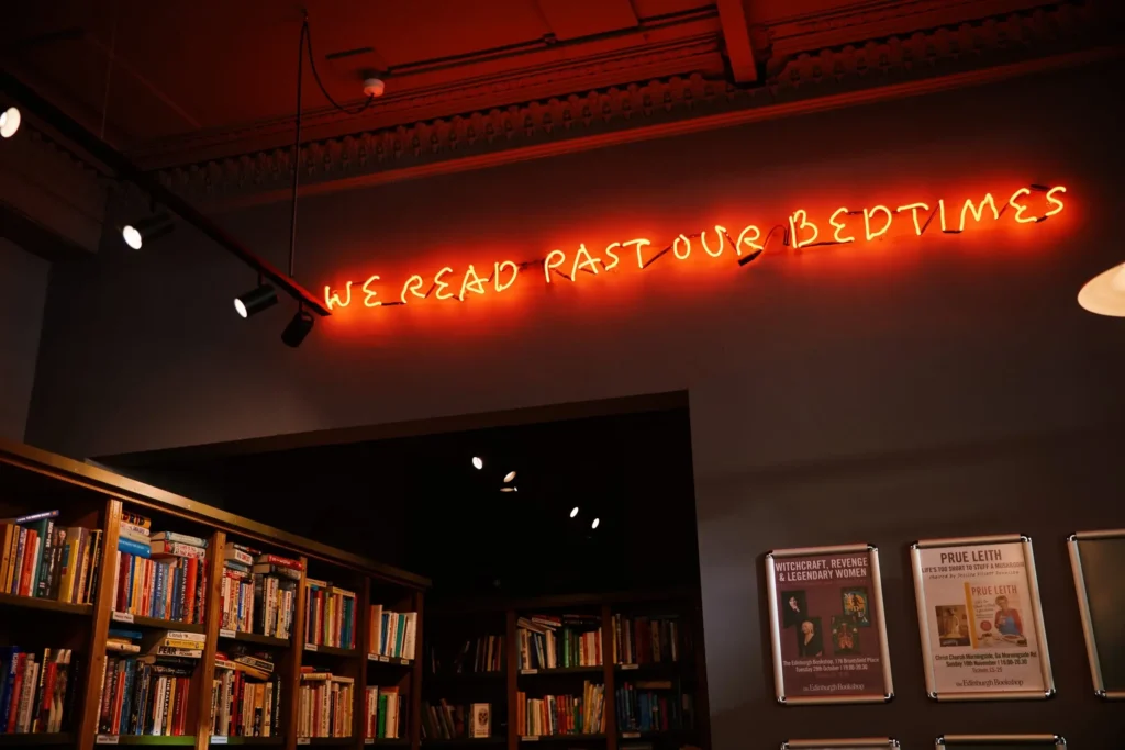 Neon sign "We read past our bedtimes" above bookshelves in The Edinburgh Bookshop.