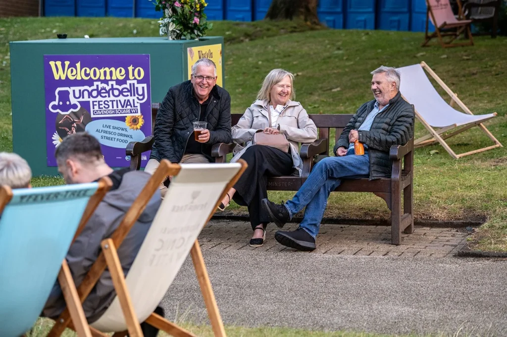 Underbelly Festival poster and smiling people on a bench at Cavendish Square.