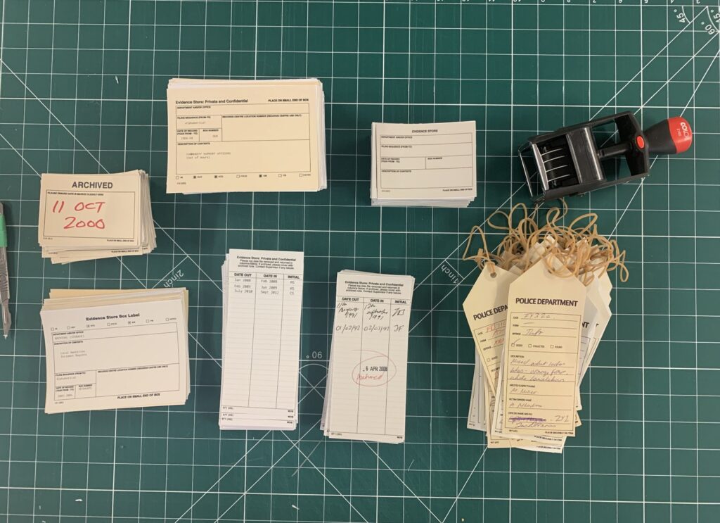 Police evidence tags, forms, and a dated "ARCHIVED" stamp on a green cutting mat.