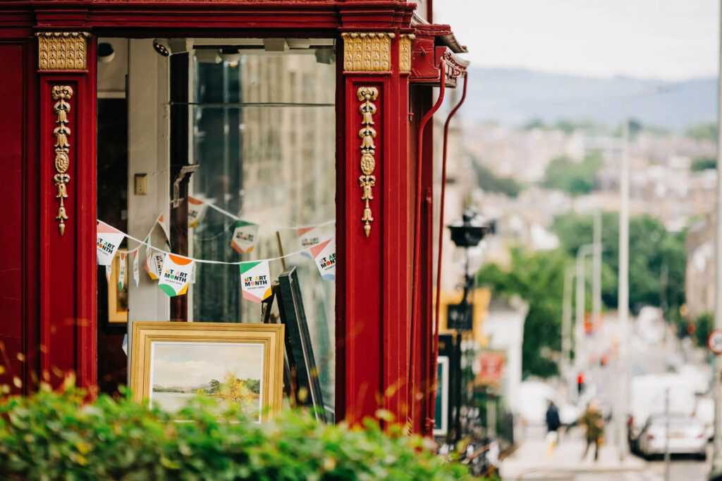 Red storefront decorated for New Town Art Month with paintings displayed