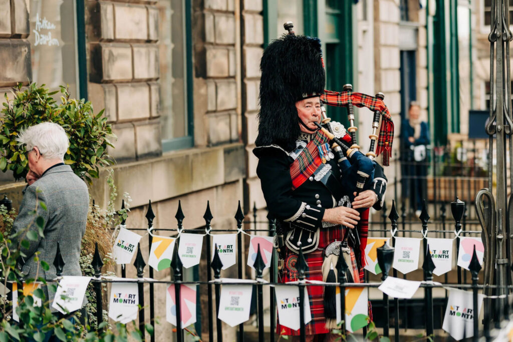 Bagpiper in traditional Scottish attire plays at New Town Art Month event.