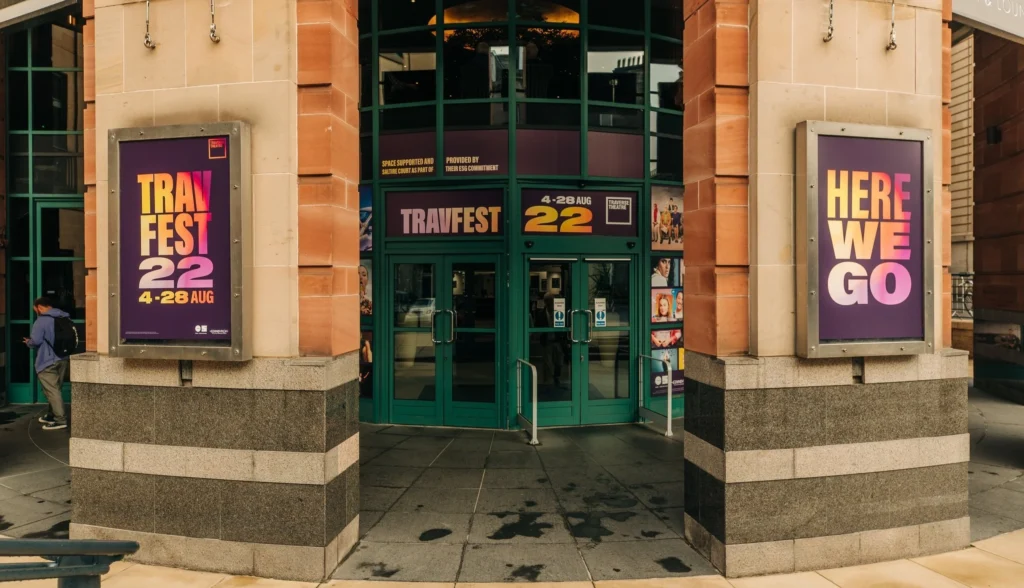 TravFest 2022 entrance with posters: "TravFest 22 4-28 AUG" and "HERE WE GO