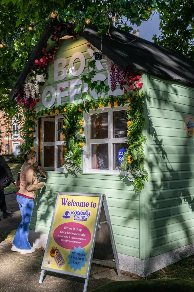 Underbelly Festival box office, a charming green booth decorated with flowers and a sign for "Disney in Drag.