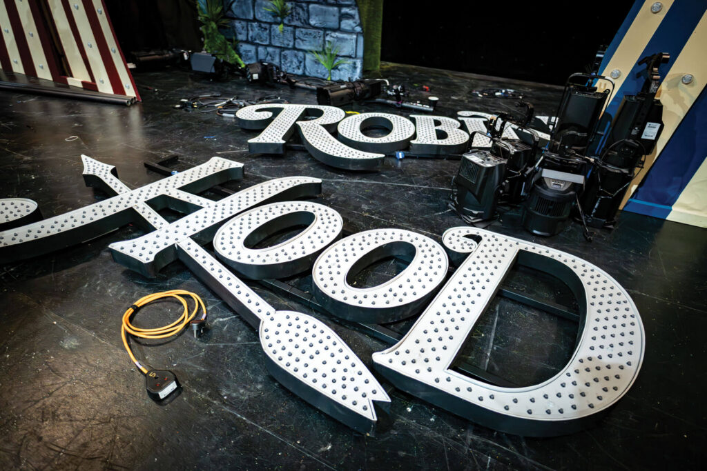 Large illuminated "Robin Hood" marquee letters on a dark stage floor.