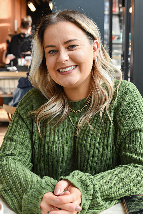 Laura Whitehouse, freelance graphic designer, smiles warmly in a cozy cafe.