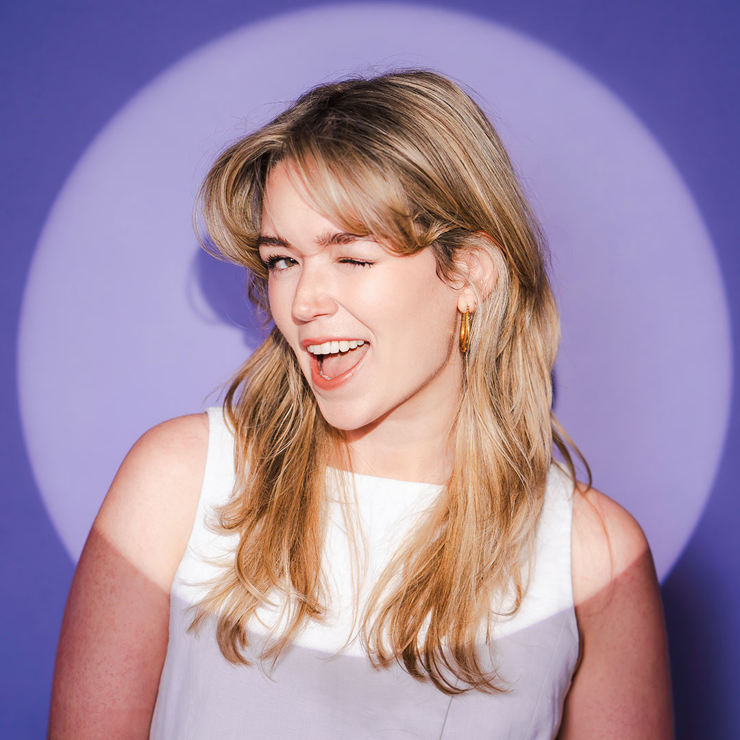 Laura Whitehouse, a freelance graphic designer, winks playfully against a purple backdrop.