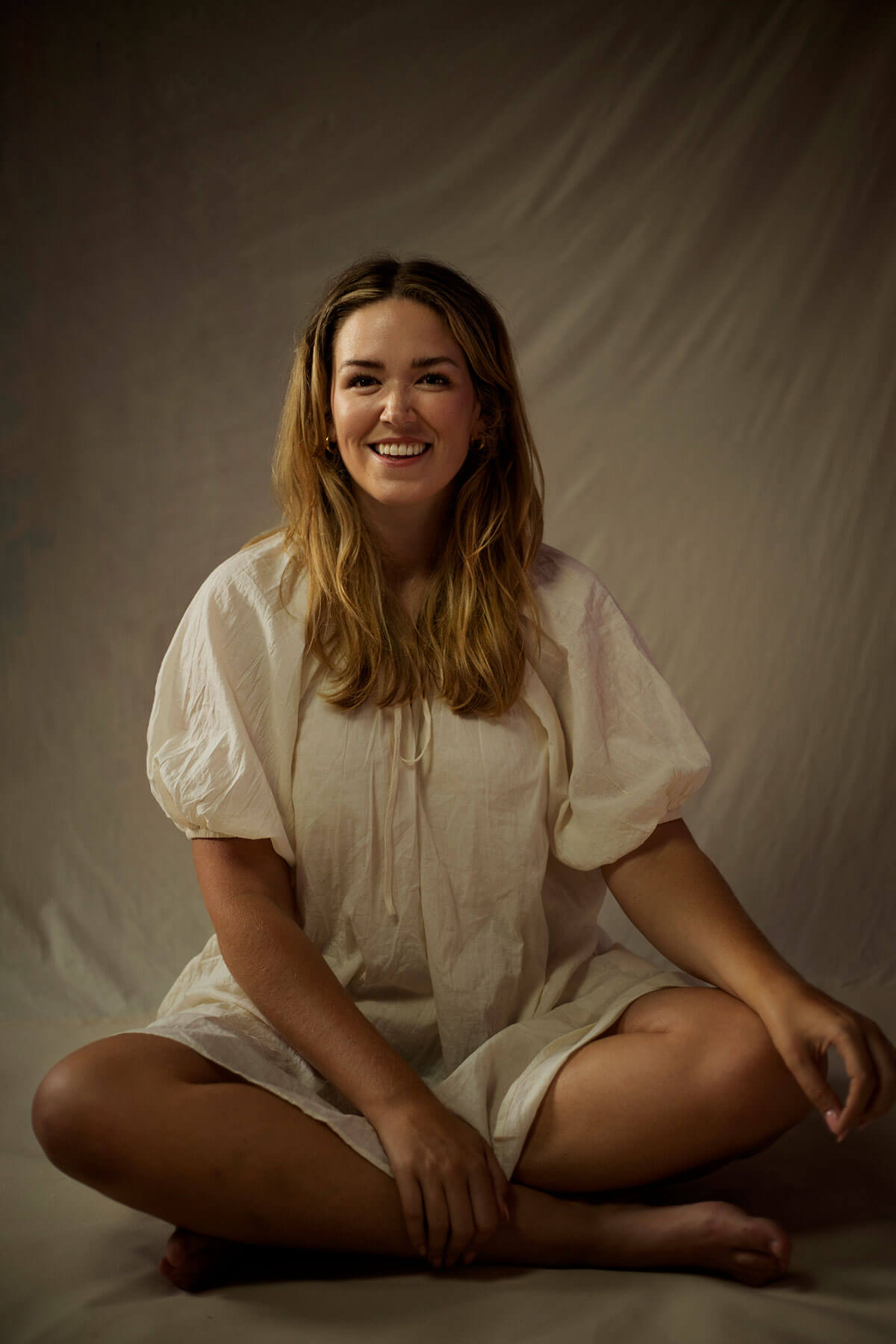 Laura Whitehouse, freelance graphic designer for theatre and film, smiles cross-legged.