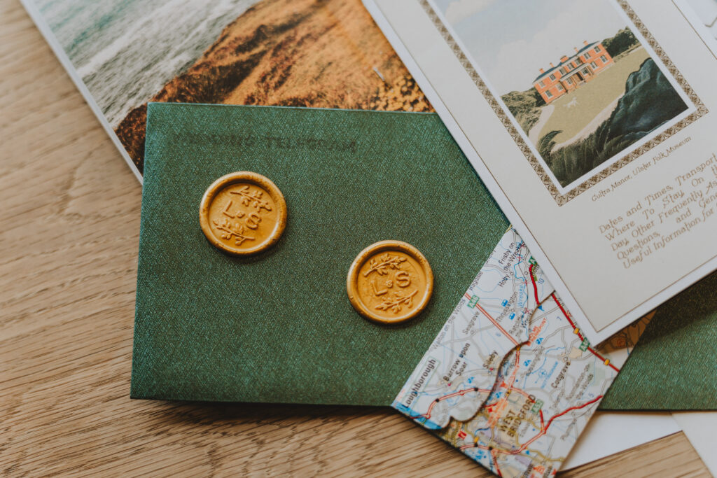 Green invitation envelope with wax seals, map, and postcard of a manor
